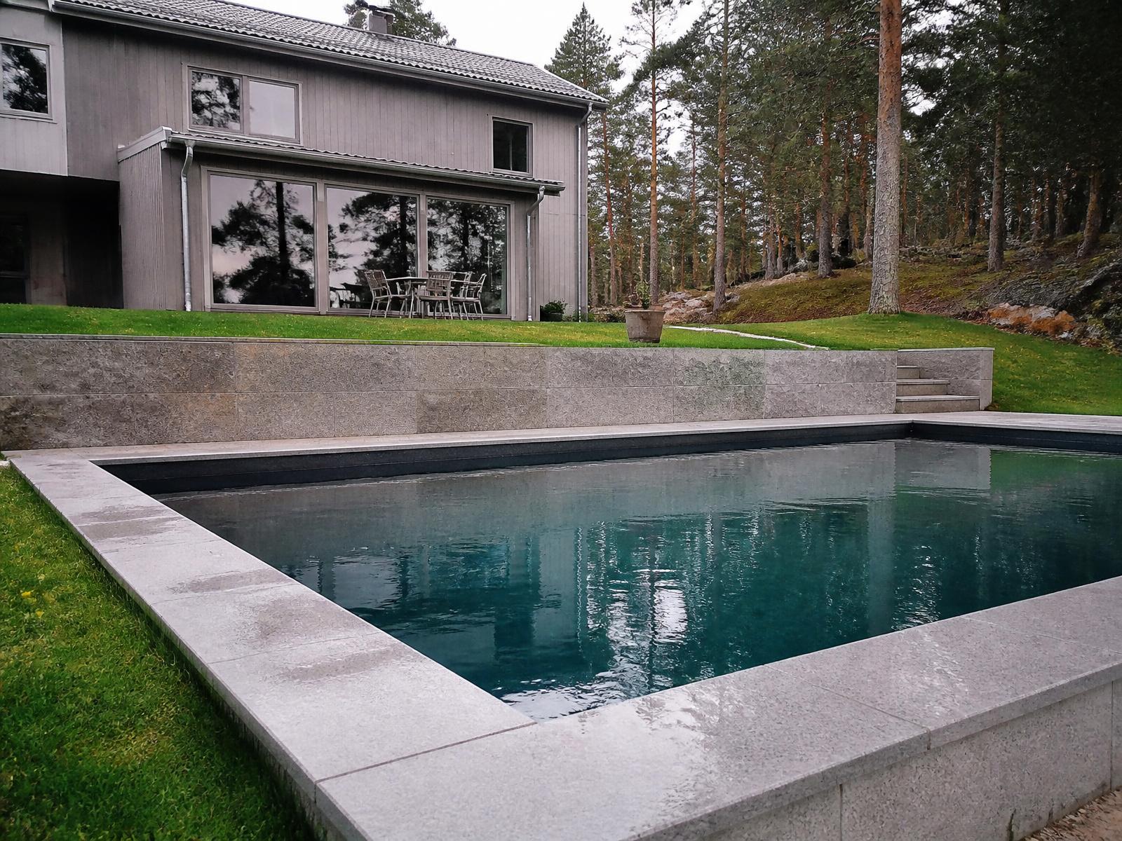 Platsbyggd betongpool med stenkant intill en modern putsad villa