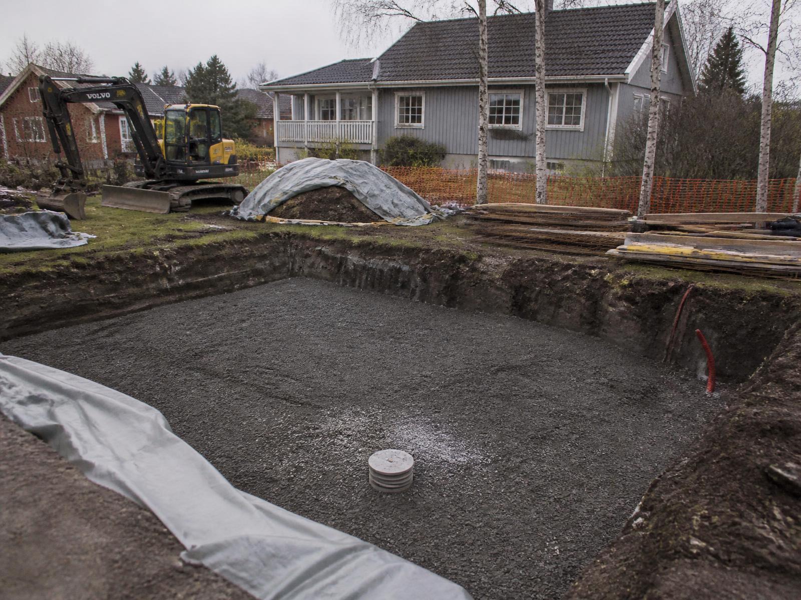Poolbyggare som installerar ett poolskal i en utgrävd trädgård