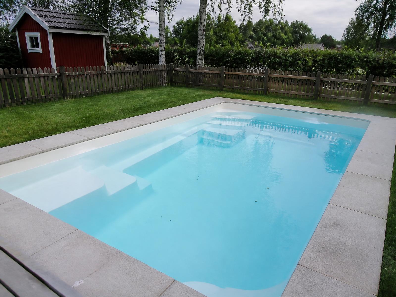 Glasfiberpool med sömlöst skal och klart turkost vatten vid ett trädäck